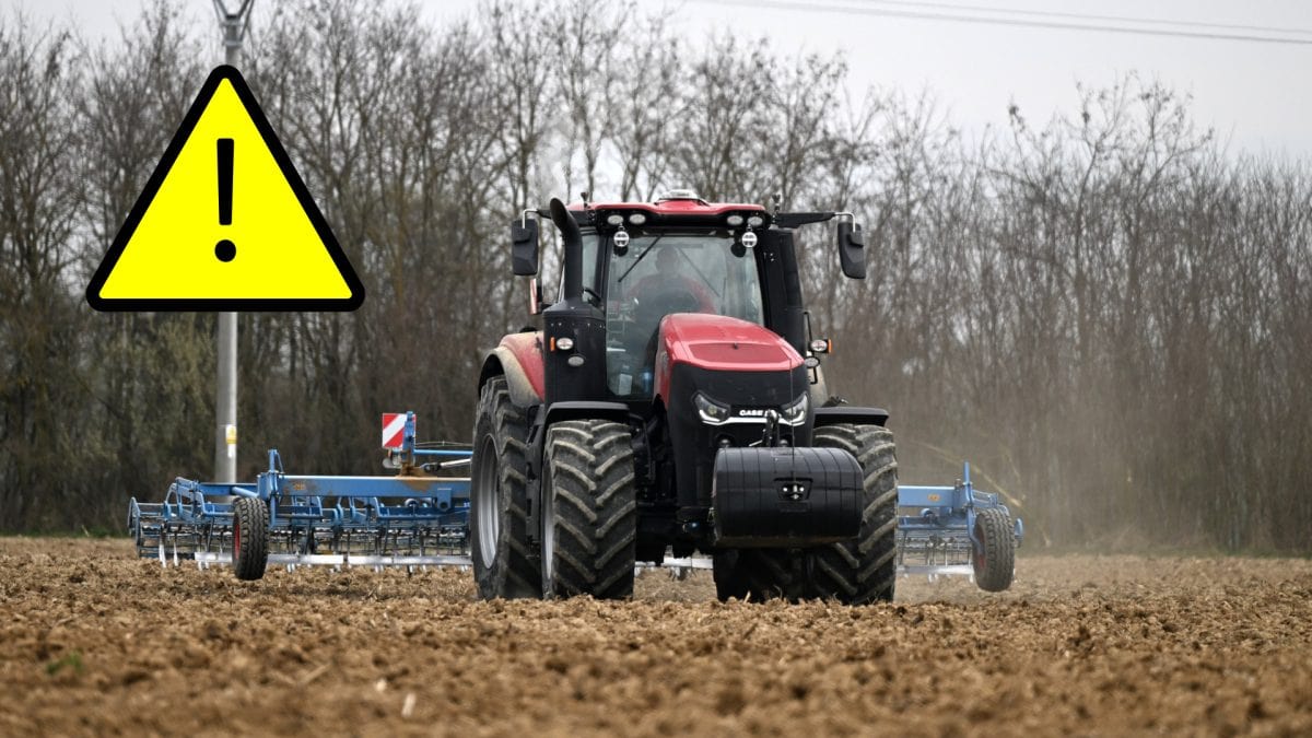 traktor obrábajúci jarnú pôdu a výstražný trojuholník